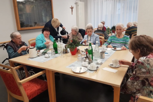 Mehrere ältere Menschen sitzen an einem Tisch und trinken aus Tassen, eine Person schenkt Kaffee aus einer Kanne ein