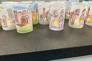 Mehrere mit mittelalterlichen Szenen bemalte Laternen aus Papier stehen auf einer dunklen Oberfläche