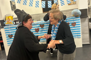Zwei Personen tanzen in einem Raum mit blau-weißer Dekoration und Lebkuchenherzen an der Wand