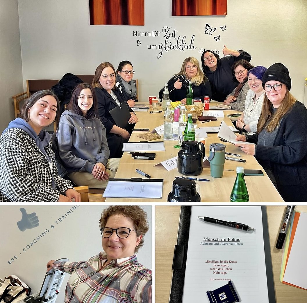 Gruppe von Menschen sitzt an einem langen Tisch mit Getränken und Unterlagen in einem Besprechungsraum mit der Wandaufschrift 'Nimm Dir Zeit um glücklich zu sein'